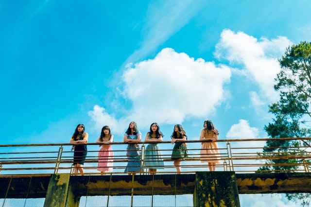 six girls leaning their elbows on the railings of a bridge